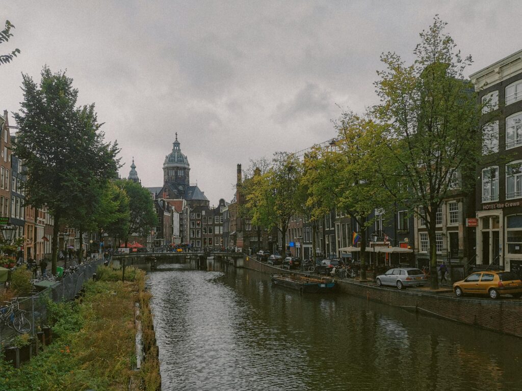 Scenic view of Amsterdam's canal with historic buildings and cathedral on a cloudy day.